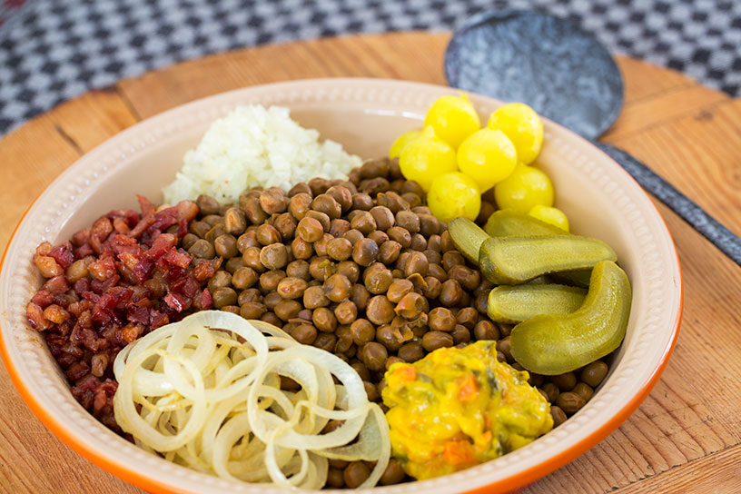 Avondeten op een bord: ui, augurk, zilveruitjes, rijst, kapucijners, spekblokjes en piccalilly